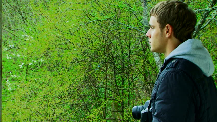 A young man with a camera photographing beautiful green scenery.
