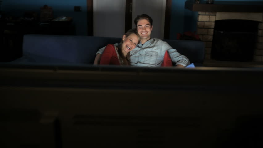young heterosexual couple watching comedy movie at home on sofa and laughing. Crane shot