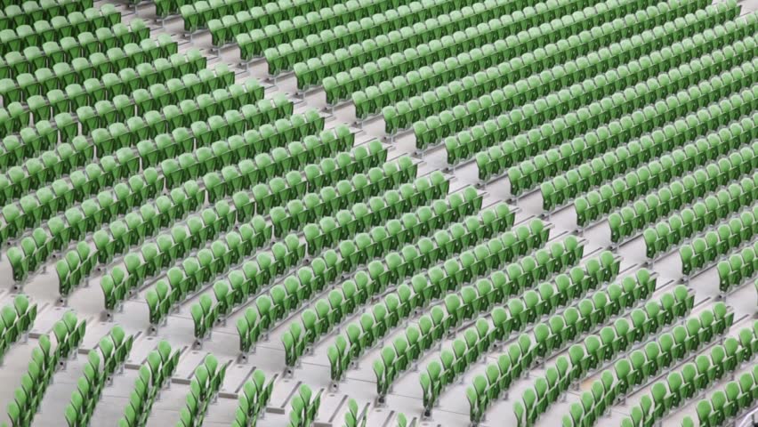 Many rows of green, plastic, folding seats in a big empty stadium.