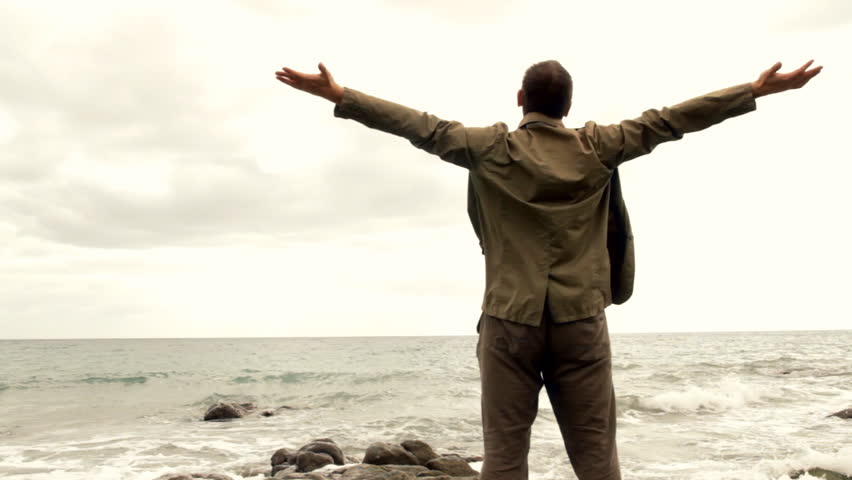 Man at the beach rising hands to the sky