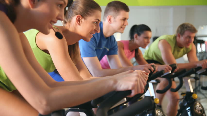 Group of five people - men and women -  in gym or fitness club exercising their legs doing cardio training