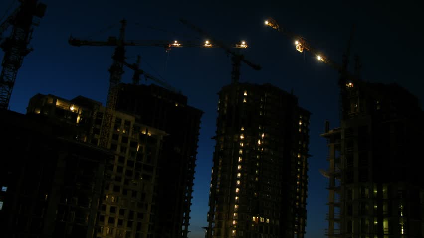 Cranes work on construction site after sunset, time lapse