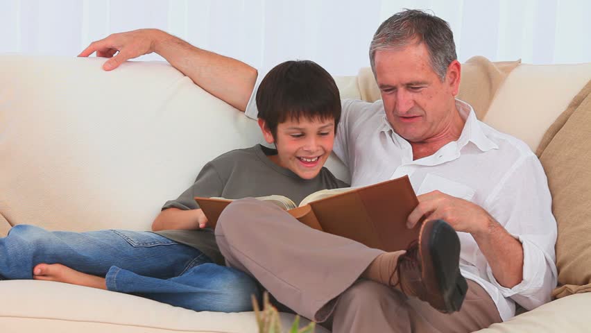 A boy looking at an album with his grandfather on the couch