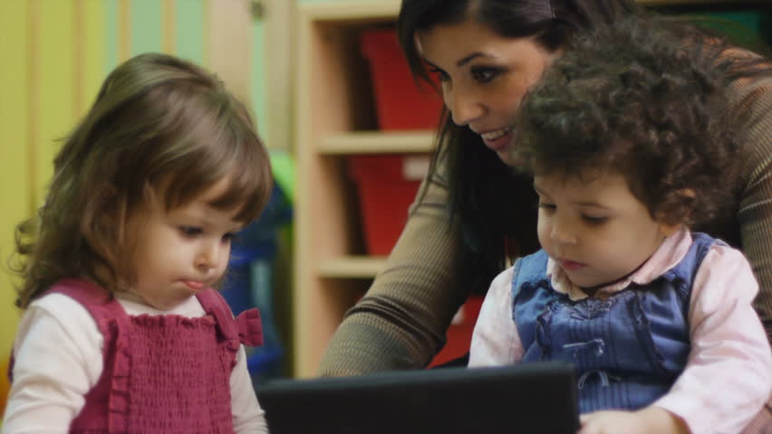Educator and little girls playing with touch pad computer in kindergarten