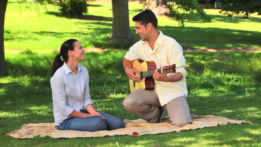 Nice man playing guitar with a rose between the teeth next to his wife