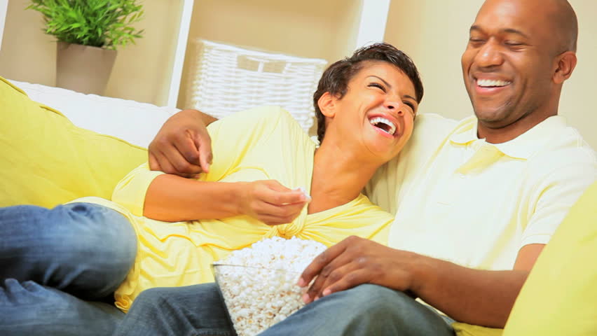 Young ethnic couple relaxing on the sofa eating from a bowl of popcorn