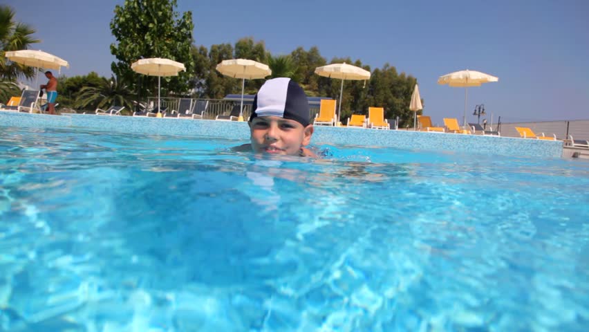 Boy in swimming cap in the pool water, the camera goes under water, and shows how he floats 