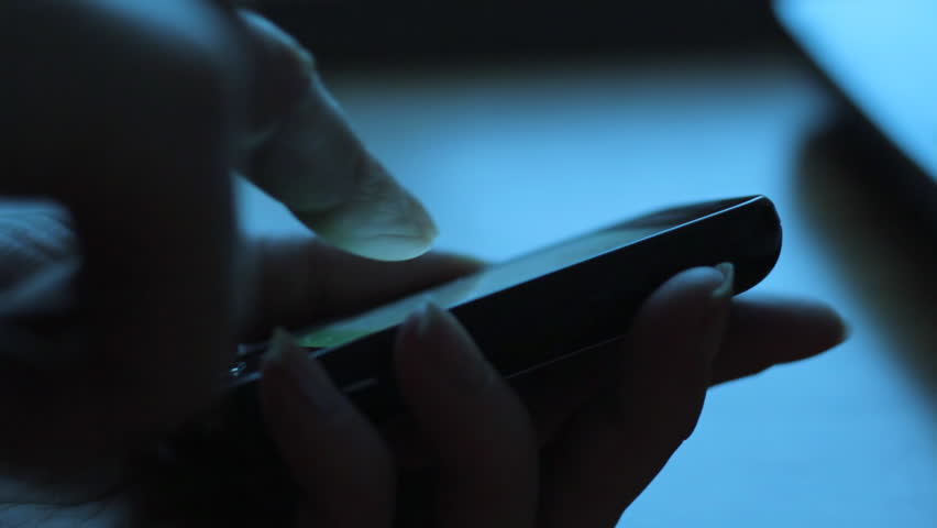Close up of woman using smartphone in dark environment, her hand dimly lit by phone screen