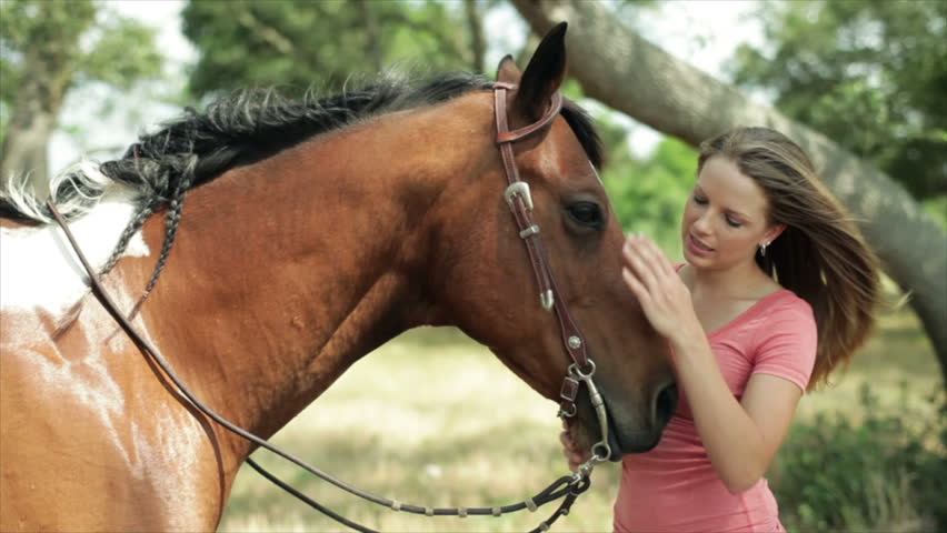 A pretty girl outside on a very windy summer day lovingly petting her beautiful horse.