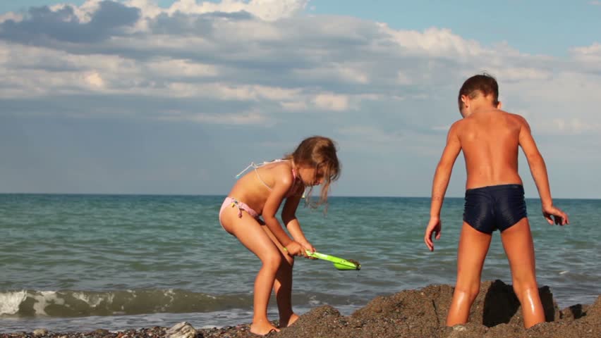 Boy and girl digging a hole in the sand, the boy took the bucket and took some water into the sea