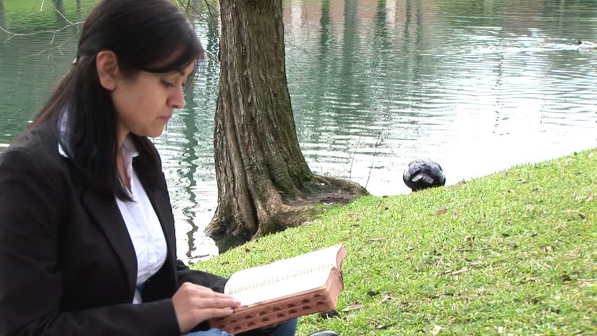 Reading the bible, lifts it to her heart.
