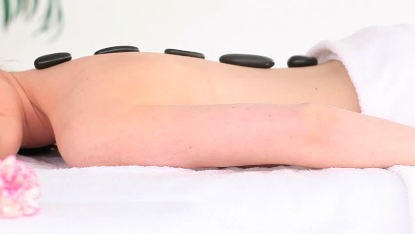 Good looking woman relaxing with pebbles on her back while lying on a towel in a spa center