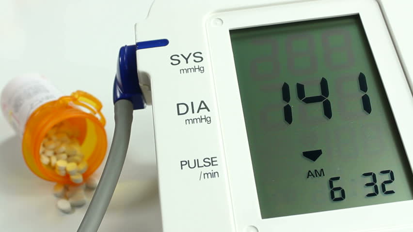 Bottle of prescription pills spills out onto table next to blood pressure monitor displaying patient readings. 1080p