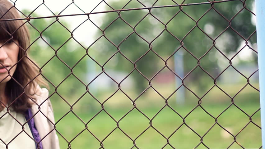 Sad woman behind chain-link fence, outdoors, dolly shot 