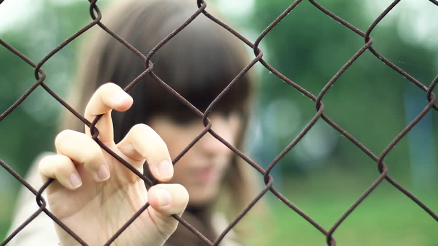 Sad woman behind chain-link fence, outdoors 