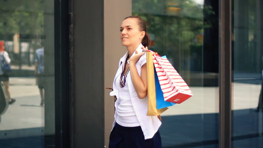 Woman with shopping bags walking by the shop window, camera stabilizer shot, slow motion