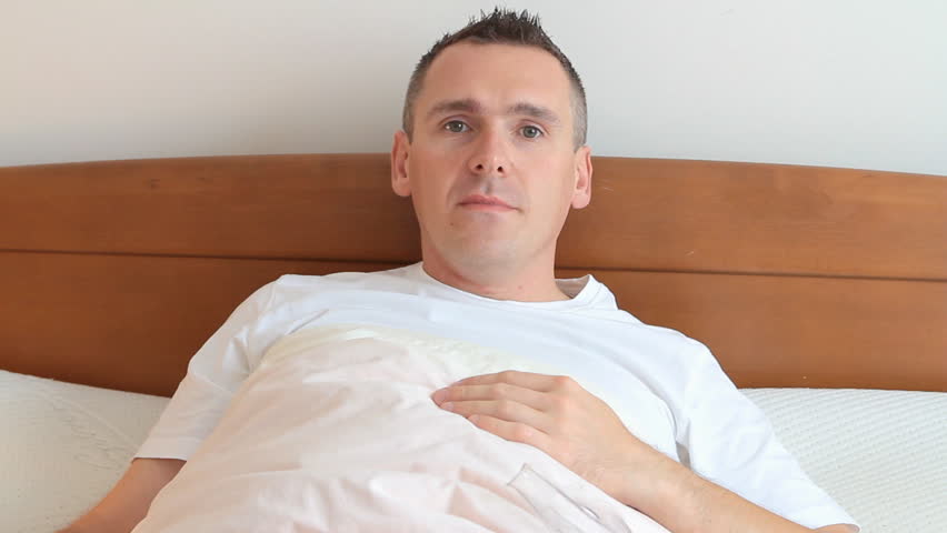Ill man with a flu coughing, using hand tissue and using inhaler also called nebulizer laying in his bed in home