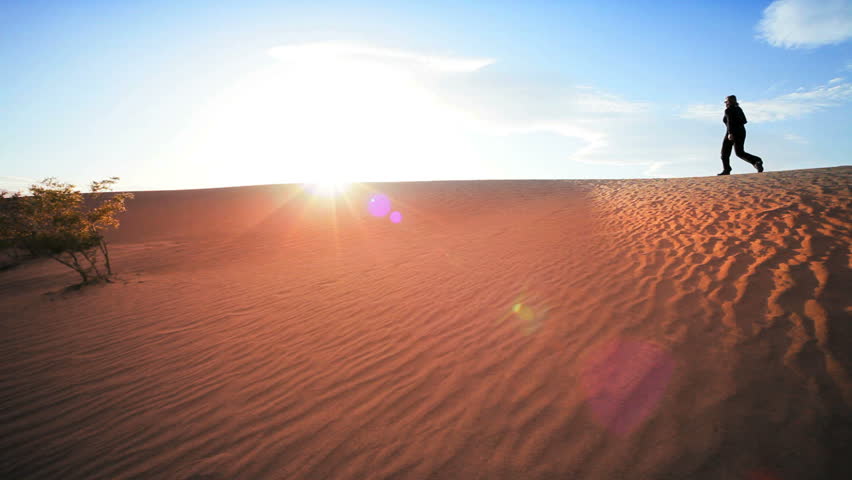 Solitary female hiking across sand dunes in a desert environment
