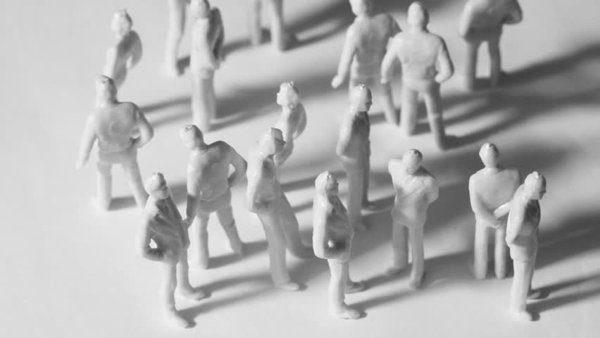 Group of little unpainted toy people stand and drop shadows, composition rotates, view from above
