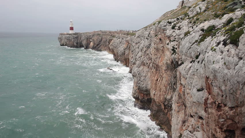 Lighthouse on the tip of the Straights of Gibraltar, Europa Point. Mediterranean Sea ocean waves crashing against rock and cliff. Red and white lighthouse stands tall as warning for ship to navigate.