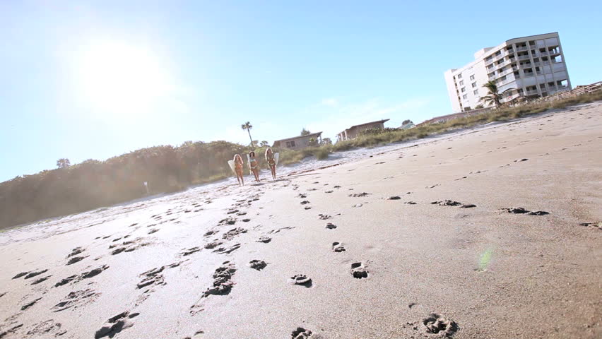 Three beautiful girlfriends with surfboards running down the beach to the ocean