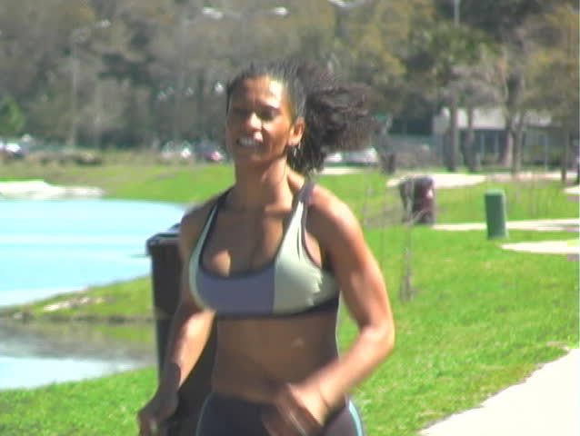 A beautiful woman with remarkable muscle definition jogs outdoors on a bright, sunny day.