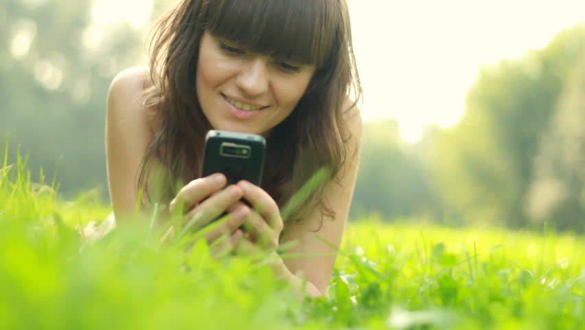 Young woman lying on the grass and sending sms, texting in the park
