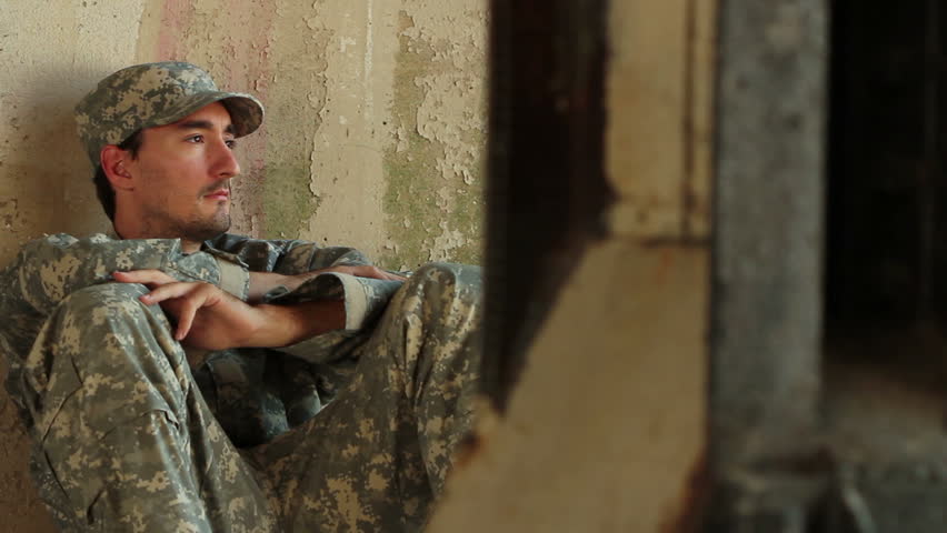 Distraught soldier sitting against concrete wall