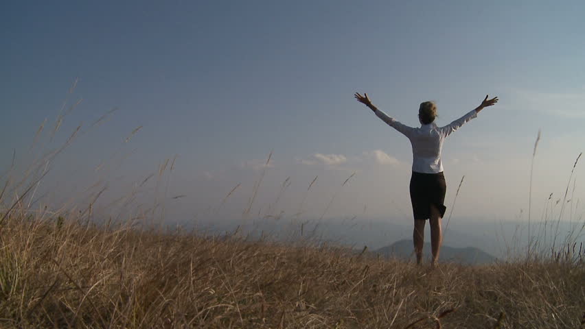 Business woman standing on cliff's edge and looking to a sky with raised hands.