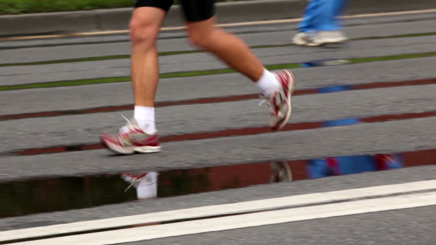 Man naked legs run in jogging shoes on asphalt with puddles, focus on front foot