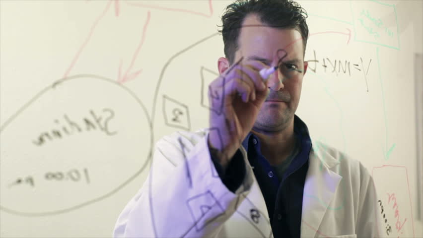 A scientist or chemist writes out a formula on a large transparent board.