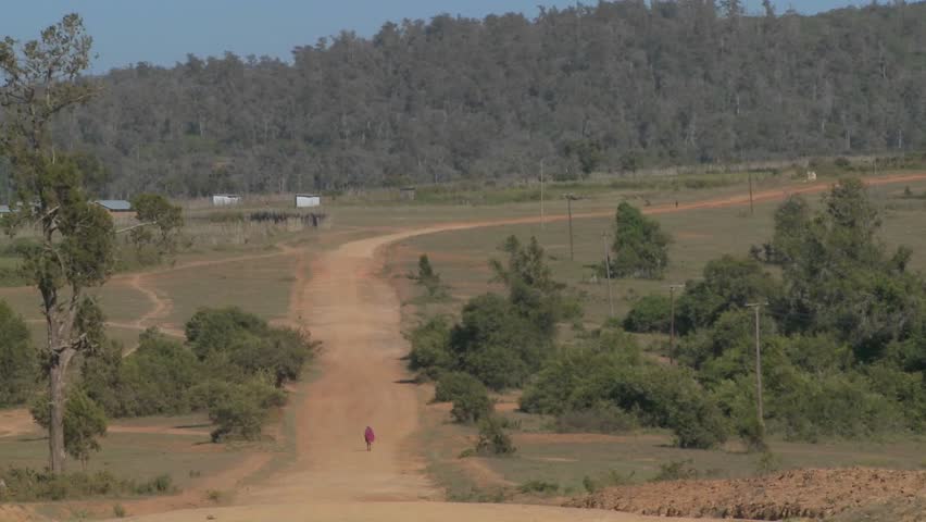A man walks in the distance on a lonely dusty dirt road in Africa.