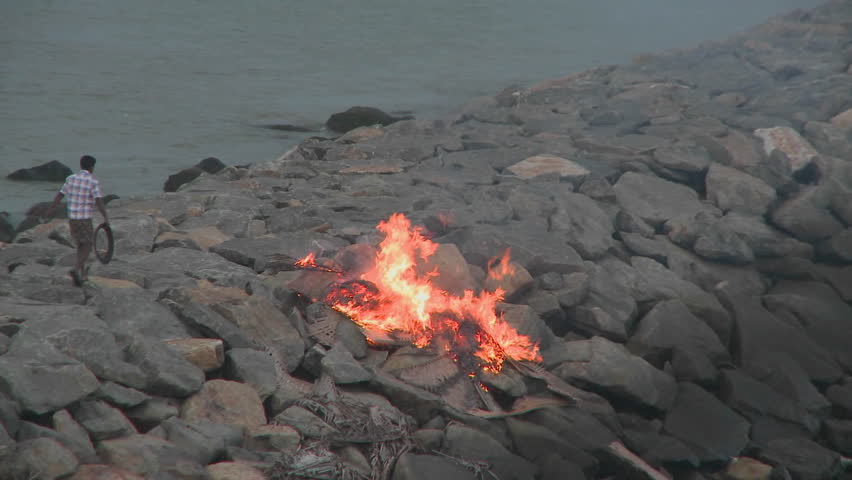 INDIA - CIRCA 2010: A man throws a piece of rubbish into a burning fire circa 2010 in India. Water supply and sanitation in India continue to be inadequate, despite longstanding efforts by the various levels of government and communities at improving cove