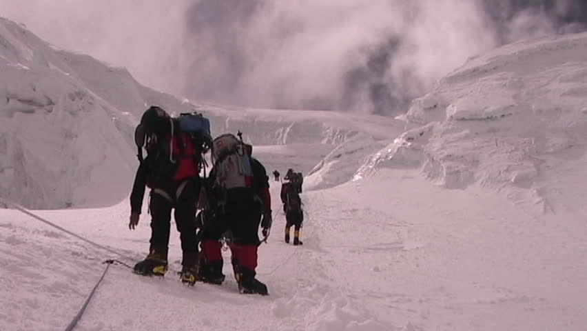 A team of climbers ascends an icy slope on Mt. Everest as clouds roll across the sky above