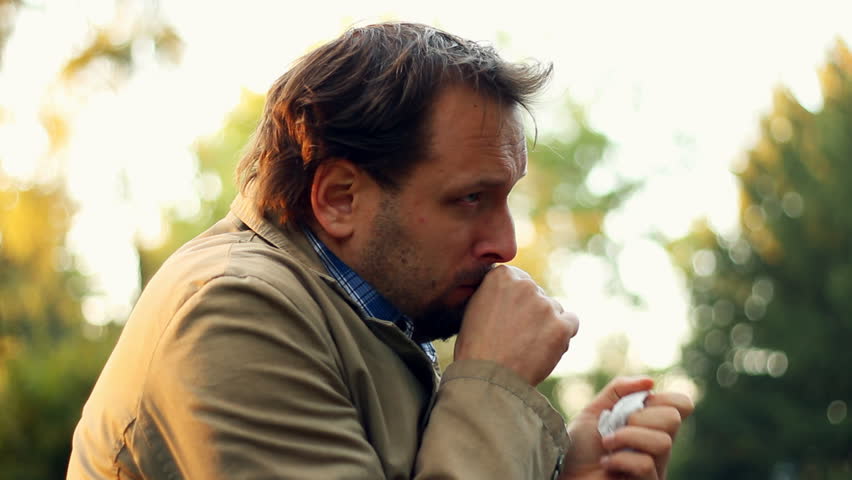 Sick man blowing his nose into tissue, outdoors