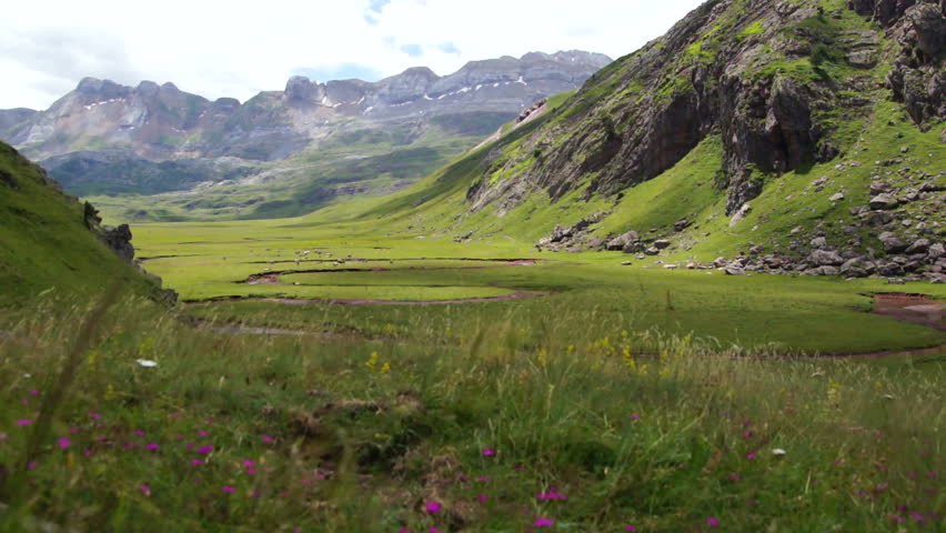 Grass fields in the Pyrenees with mountains in the background.
