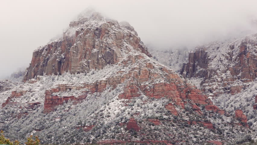 Clouds move slowly over the newly snowed red rocks in scenic Sedona, Arizona.