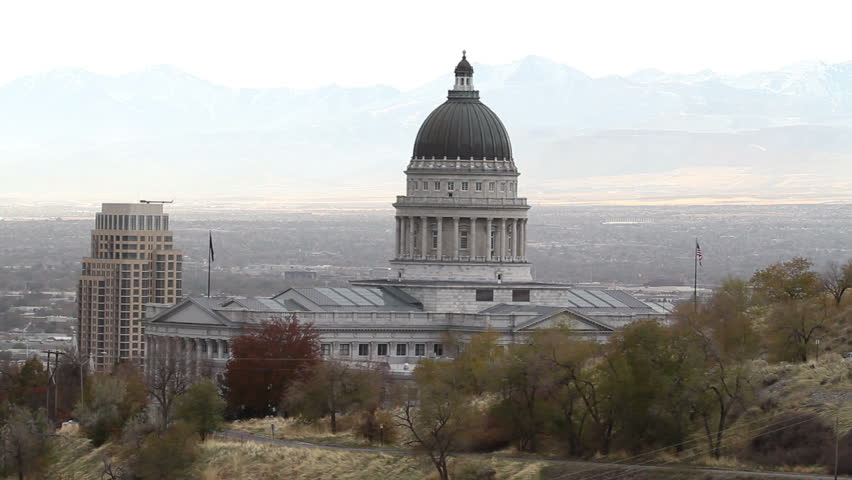 Utah State Capital from mountain looking past dome into valley and Salt Lake City. Normal haze from city. Traffic on mountain road leading to building.