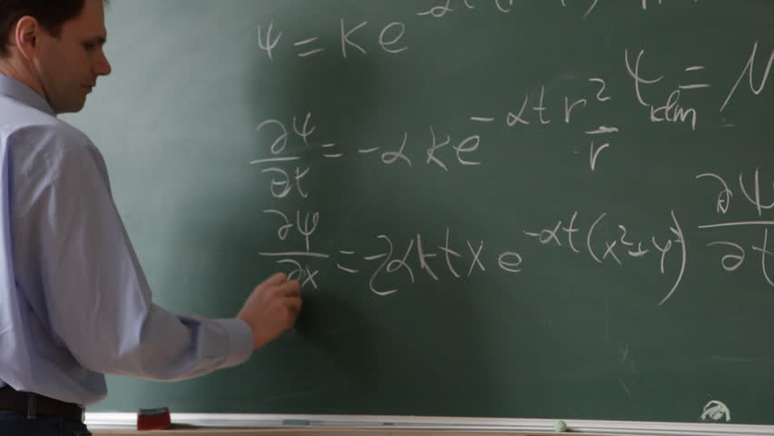 Lecturer in jeans and blue shirt writing formulas on a chalkboard in university