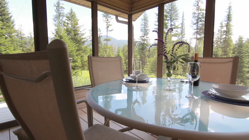Slider dolly shot of a table with wine and wine glasses in a sun room with a pine tree forest outside