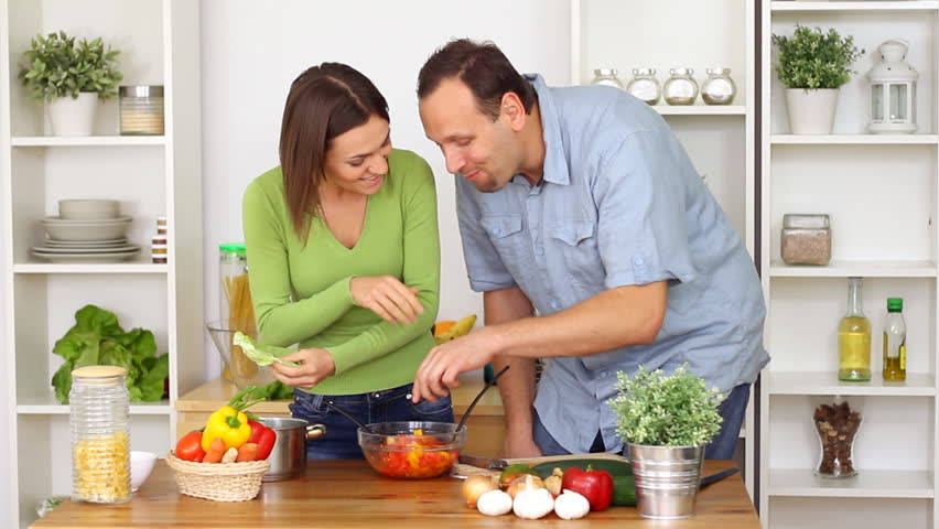 Young happy couple preparing and tasting salad in the kitchen 