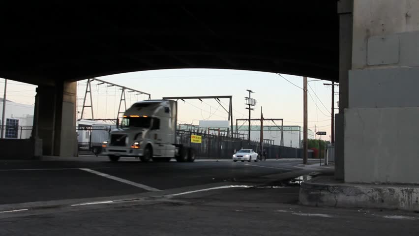 Underneath and overpass with a semi truck and two bicycle cops passing by.