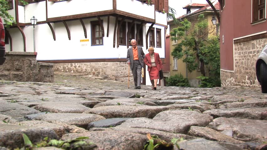 PLOVDIV, BULGARIA - CIRCA MAY 2007: An elderly couples walk across a cobblestone street circa May 2007 in Plovdiv.