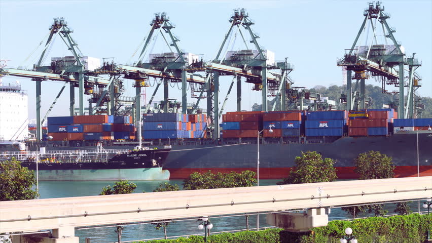Singapore - November 25, 2009: (Timelapse View) Gantry cranes work at a large freighter at PSA industry harbor in Singapore. The Sentosa monorail passes in the foreground. Photo time-lapse (tight shutter).