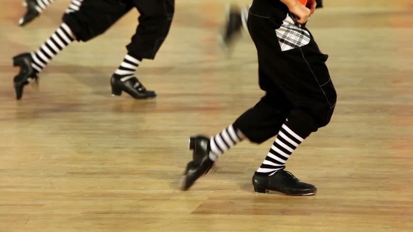 Few boys in shoes with taps, black pants and striped socks tap dance, only legs are visible