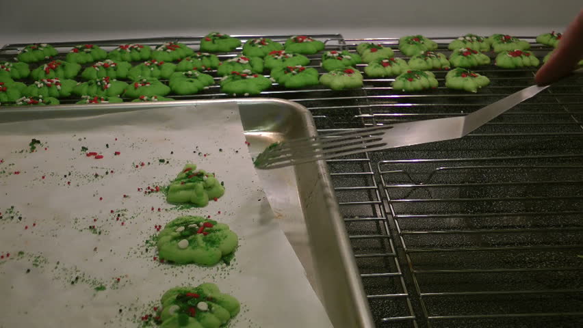 HD of yummy fresh baked spritz tree cookies hot from the oven being removed with a spatula from the parchment lined cookie sheet and placed on a cooling rack