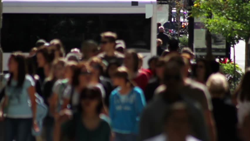 Telephoto shot with a backlit crowd of people walking on a wide sidewalk