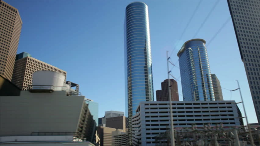 The amazing architecture of skyscrapers and high rise office buildings of downtown Houston Texas appear to turn gently against the bright blue sky as one drives past on the nearby interstate highway.