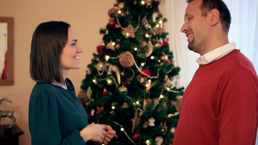 Man giving gift to woman in front of Christmas tree