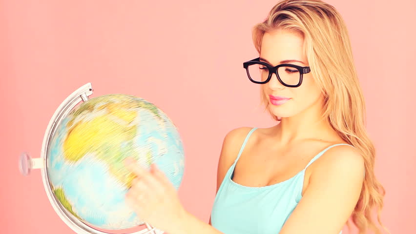 Laughing blonde woman in oversized glasses playing with a world globe, concept spoof for a studious person.